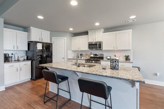 kitchen with visible vents, appliances with stainless steel finishes, tasteful backsplash, a sink, and a breakfast bar