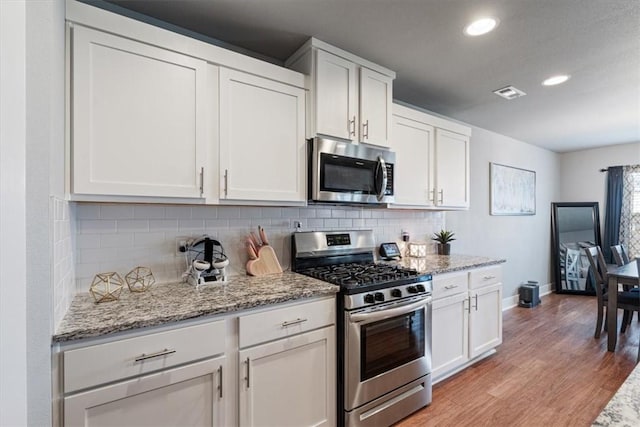 kitchen with appliances with stainless steel finishes, light wood finished floors, white cabinetry, backsplash, and visible vents