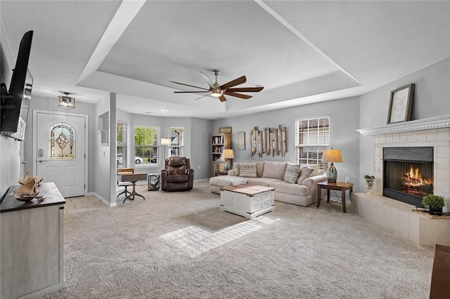 carpeted living area featuring baseboards, a tray ceiling, ceiling fan, and a tile fireplace