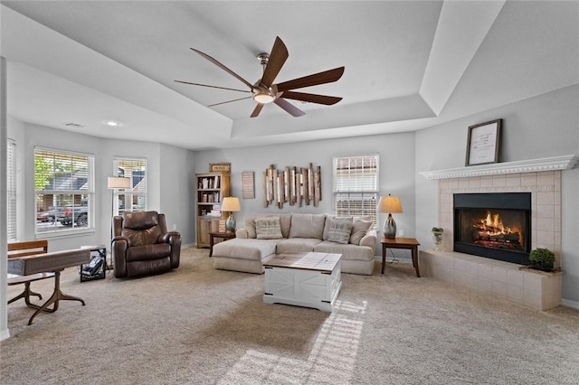 carpeted living room featuring ceiling fan, a raised ceiling, and a tile fireplace