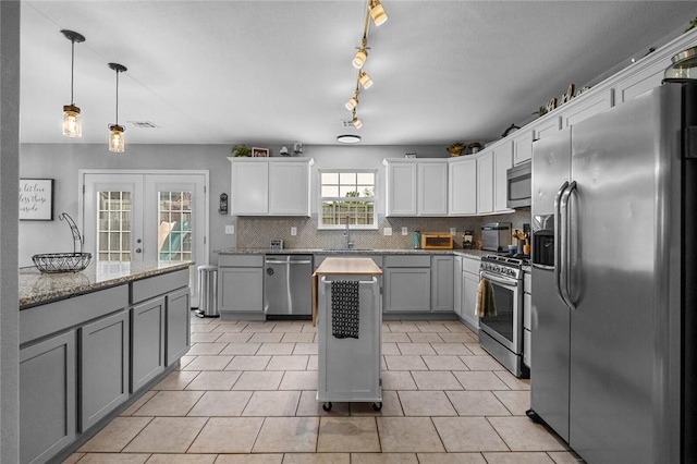 kitchen with pendant lighting, tasteful backsplash, gray cabinetry, white cabinets, and stainless steel appliances