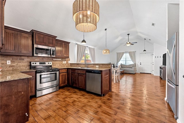 kitchen with appliances with stainless steel finishes, a sink, a peninsula, open floor plan, and lofted ceiling