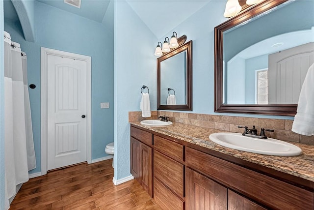 bathroom featuring a sink, double vanity, toilet, and wood finished floors