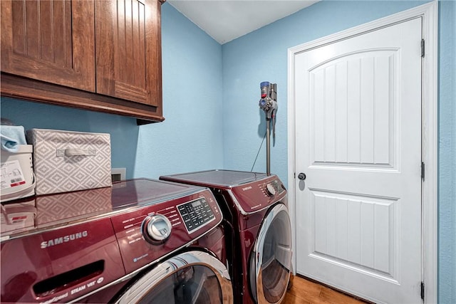 clothes washing area featuring a textured wall, washing machine and dryer, cabinet space, and wood finished floors