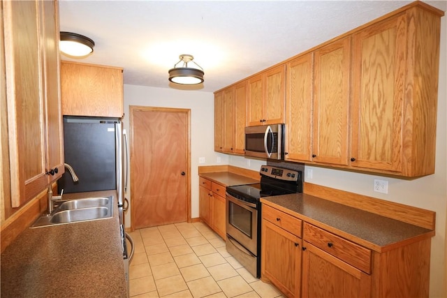 kitchen with appliances with stainless steel finishes, dark countertops, brown cabinets, a sink, and light tile patterned floors