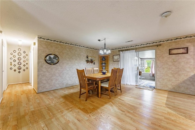 dining room featuring a textured ceiling, wallpapered walls, a chandelier, and light wood-style flooring