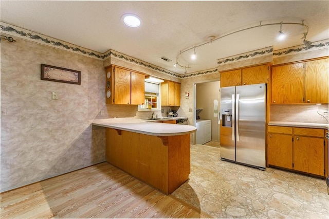 kitchen with stainless steel fridge, washer and clothes dryer, brown cabinets, and light countertops