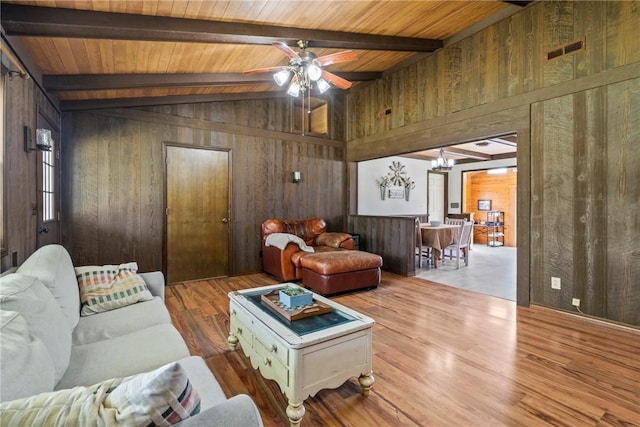 living room with visible vents, wood walls, wood finished floors, vaulted ceiling with beams, and ceiling fan with notable chandelier