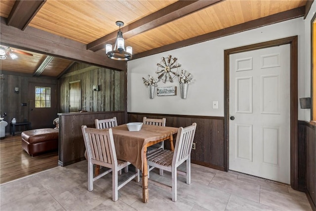 dining space featuring wainscoting, wooden ceiling, ceiling fan with notable chandelier, wooden walls, and vaulted ceiling with beams