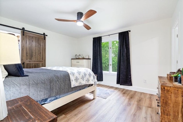 bedroom featuring a ceiling fan, baseboards, a barn door, and light wood-type flooring