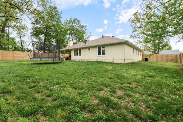 rear view of property featuring a lawn, a trampoline, and a fenced backyard