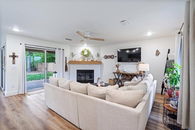 living room featuring visible vents, a glass covered fireplace, wood finished floors, baseboards, and ceiling fan