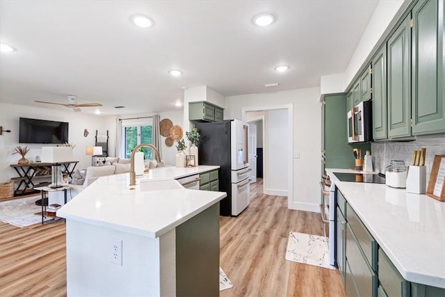 kitchen with a peninsula, light countertops, a sink, appliances with stainless steel finishes, and green cabinets