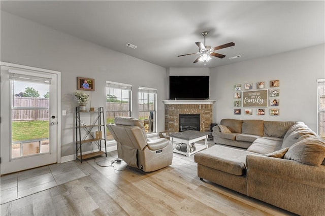 living area featuring a brick fireplace, a ceiling fan, visible vents, and light wood-style floors
