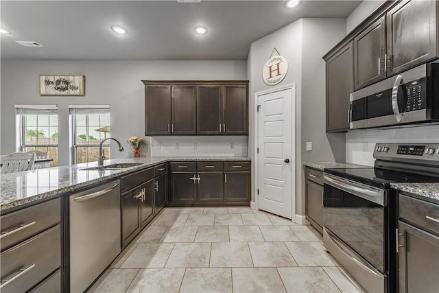 kitchen with visible vents, appliances with stainless steel finishes, dark brown cabinets, a sink, and light stone counters