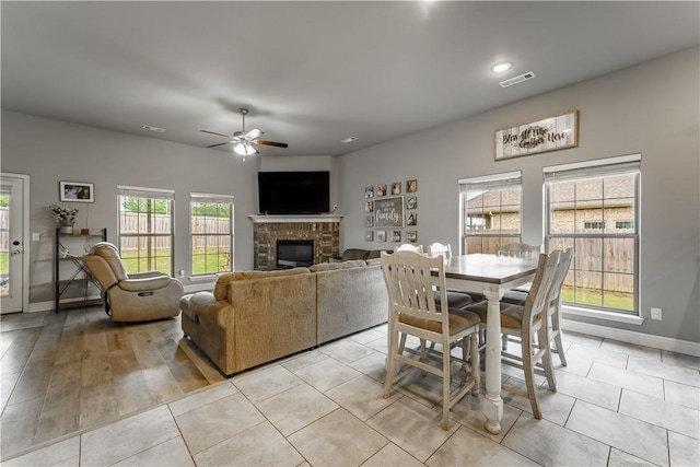 dining room with a ceiling fan, visible vents, a brick fireplace, light tile patterned floors, and baseboards
