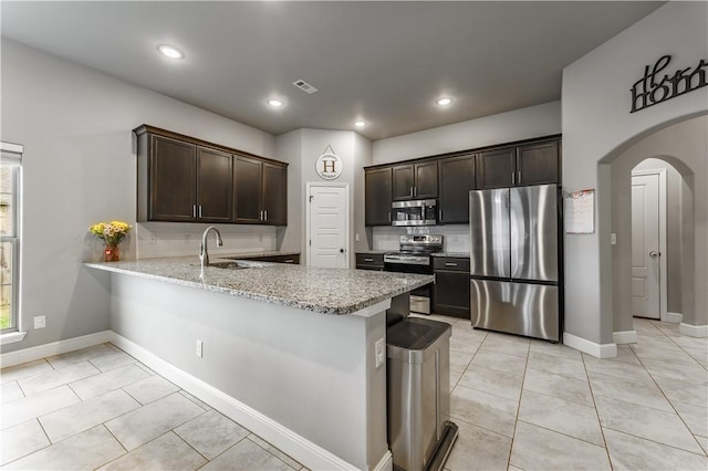 kitchen with stainless steel appliances, arched walkways, light stone counters, and dark brown cabinetry