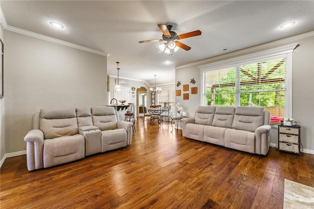 living room with dark wood-style flooring, visible vents, baseboards, ceiling fan with notable chandelier, and ornamental molding
