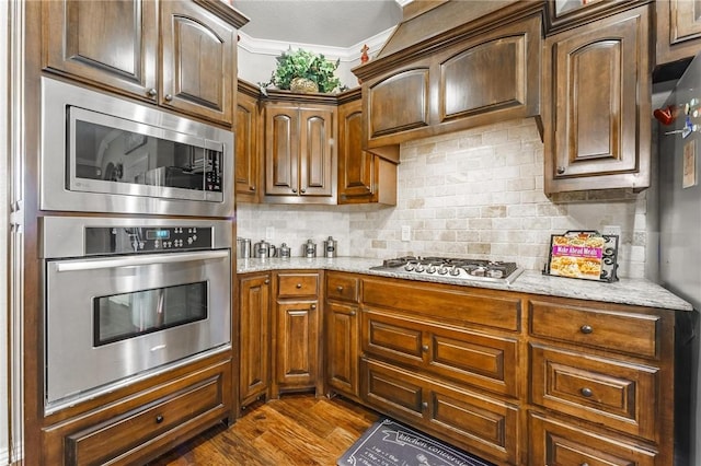 kitchen featuring dark wood-type flooring, decorative backsplash, appliances with stainless steel finishes, and light stone countertops