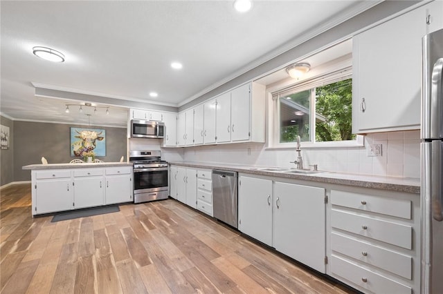 kitchen featuring appliances with stainless steel finishes, a sink, white cabinetry, light wood-type flooring, and ornamental molding