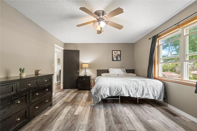 bedroom featuring ceiling fan, a textured ceiling, baseboards, wood finished floors, and visible vents