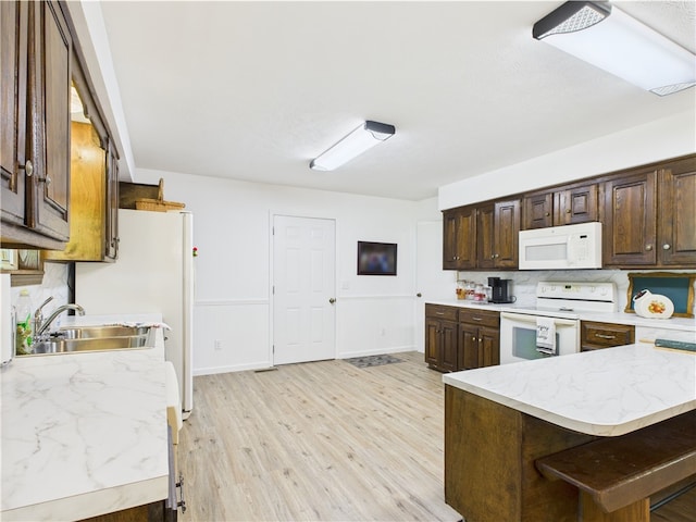 kitchen featuring dark brown cabinets, a sink, white appliances, baseboards, and light wood-type flooring