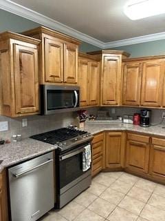 kitchen with crown molding, appliances with stainless steel finishes, light countertops, brown cabinetry, and light tile patterned floors
