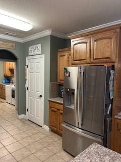 kitchen featuring ornamental molding, brown cabinets, stainless steel fridge with ice dispenser, arched walkways, and light tile patterned floors
