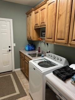 laundry room with cabinet space, light tile patterned flooring, a sink, baseboards, and washer and clothes dryer