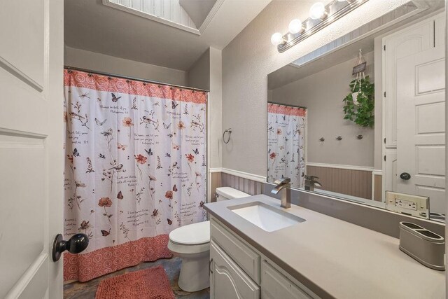 bathroom featuring a wainscoted wall, vanity, toilet, and a shower with shower curtain