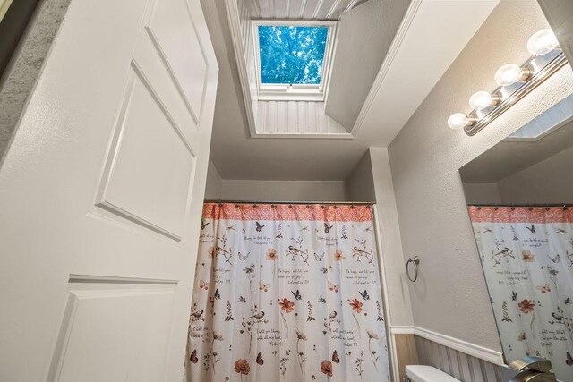full bath with a skylight, a textured wall, wainscoting, and curtained shower