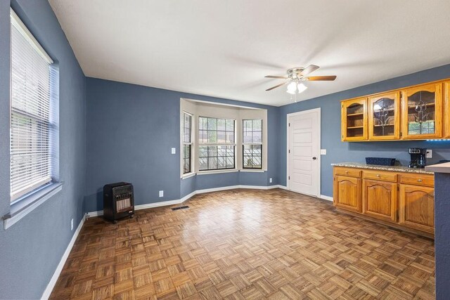 interior space featuring ceiling fan, visible vents, a wood stove, baseboards, and heating unit