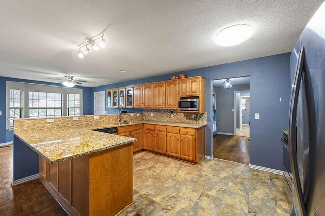 kitchen featuring brown cabinets, appliances with stainless steel finishes, a sink, a peninsula, and baseboards