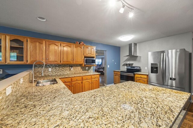 kitchen featuring a peninsula, wall chimney exhaust hood, tasteful backsplash, a sink, and stainless steel appliances