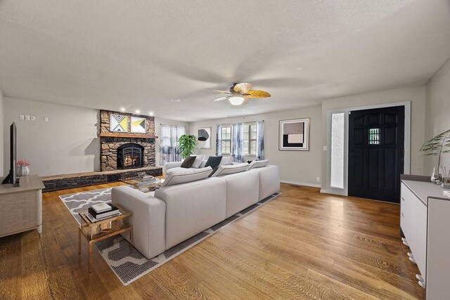 living room with a stone fireplace, a ceiling fan, a textured ceiling, and wood finished floors