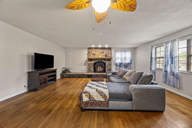 living room with baseboards, ceiling fan, a stone fireplace, and wood finished floors