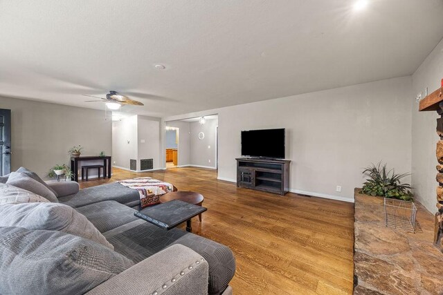 living room with a fireplace, a ceiling fan, baseboards, wood finished floors, and visible vents