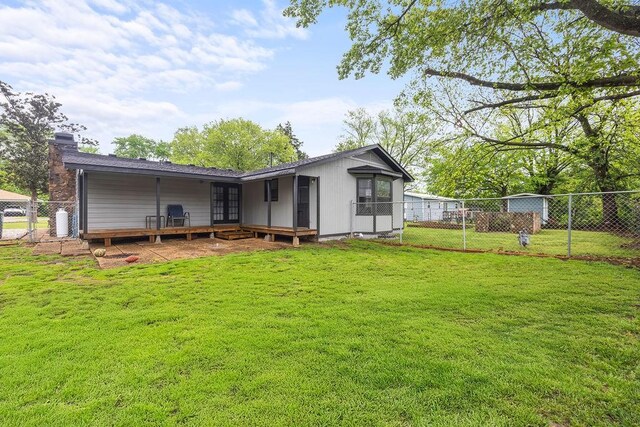 back of property with fence, a wooden deck, a chimney, french doors, and a yard