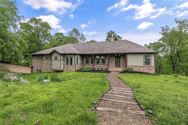 single story home featuring brick siding, a chimney, and a front yard