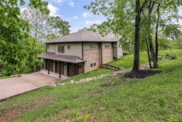 rear view of house featuring a garage, roof with shingles, brick siding, concrete driveway, and a yard