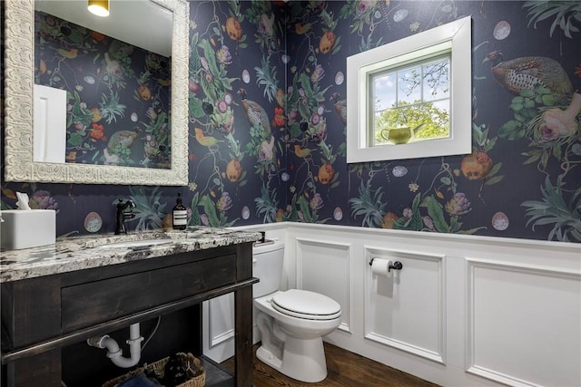 bathroom featuring a wainscoted wall, toilet, wallpapered walls, and a decorative wall