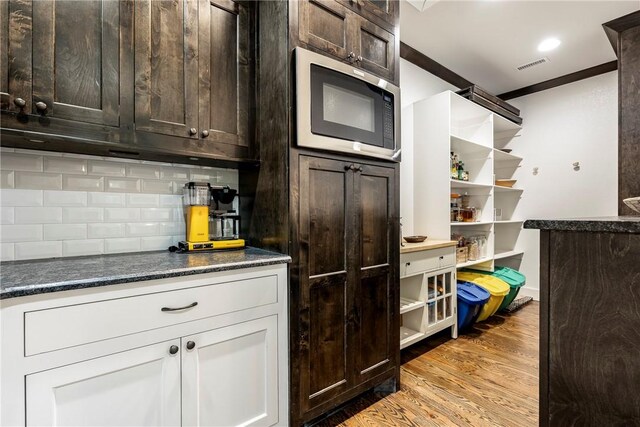kitchen featuring open shelves, tasteful backsplash, stainless steel microwave, and visible vents