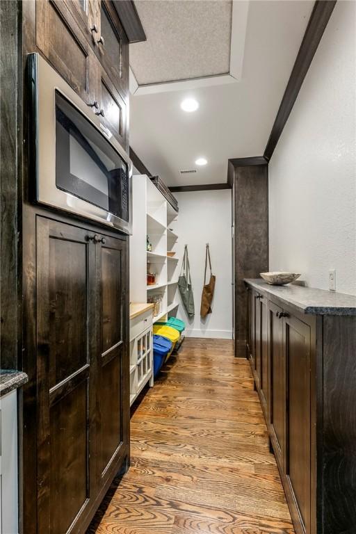 interior space with open shelves, stainless steel microwave, light wood finished floors, and dark brown cabinets