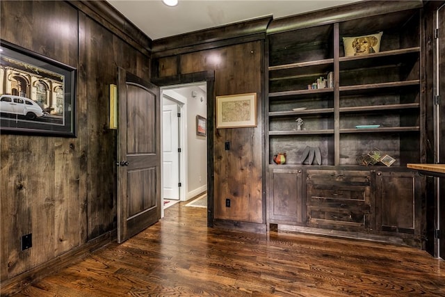 interior space featuring wooden walls, baseboards, crown molding, and dark wood finished floors