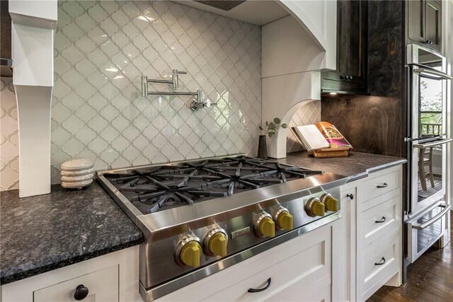 kitchen with decorative backsplash, white cabinetry, arched walkways, a warming drawer, and stainless steel appliances