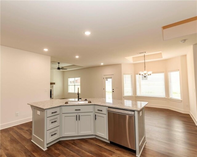 kitchen with stainless steel dishwasher, a center island with sink, dark wood finished floors, a sink, and ceiling fan with notable chandelier