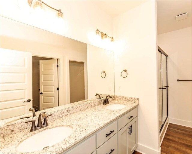 full bath with double vanity, a shower stall, a sink, and wood finished floors