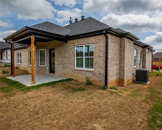 rear view of property with central air condition unit, a patio, a lawn, and brick siding