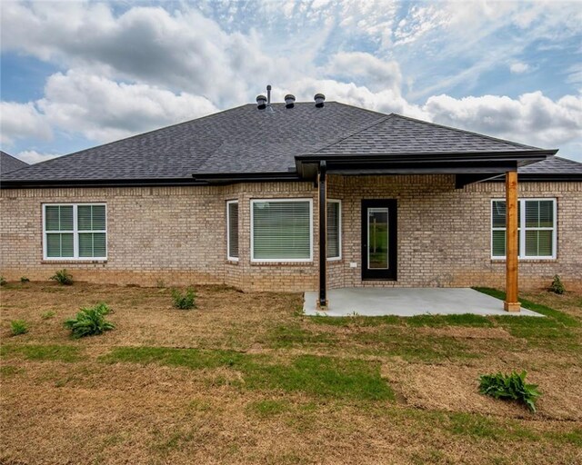 back of property featuring roof with shingles, a patio, a lawn, and brick siding