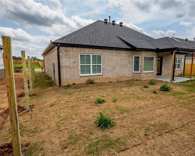 back of house with brick siding, fence, a patio, and roof with shingles